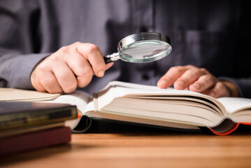 Closeup man use magnifying glass with many books on the table