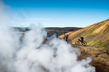 Mountain bikers walking up mountain white smoke steam in foreground, Iceland