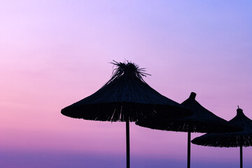 straw umbrellas during epic sunset dawn light, purple orange sky