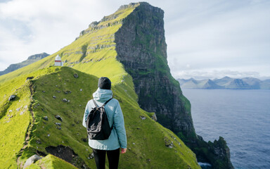 Woman traveler with a backpack enjoying the view at coast cliff edge during travel Faroe Islands....