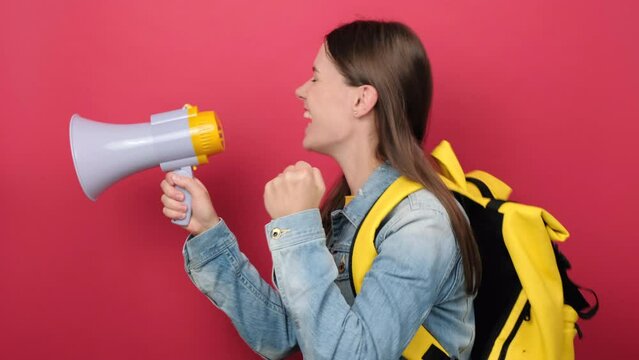 Portrait young woman student in denim jacket and yellow backpack hold scream megaphone announces discounts sale Hurry up isolated on red color background wall in studio. Education in college concept