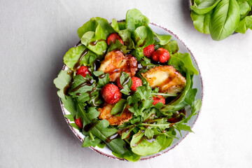 Plate with fresh salad of arugula, plants, cheese, basil and strawberry.