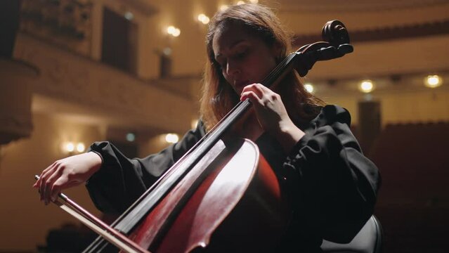 romantic woman is playing violoncello in music hall, female cellist is rehearsing on scene of philharmonic hall