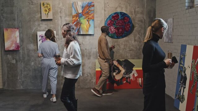 Diverse people walking and looking at paintings in contemporary art gallery at daytime
