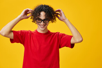 Cute attractive myopic young student man in red t-shirt hold funny eyewear posing isolated on over yellow studio background. The best offer with free place for advertising. Education College concept