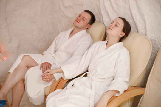 Young man and woman in a white bathrobes relaxing in a salt room