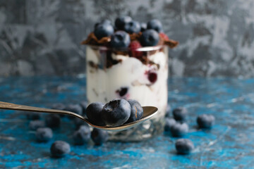 Blueberries in a teaspoon close-up and fancy delicious dessert with chocolate, yogurt and raspberry...