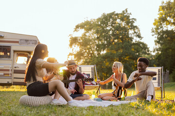 A group of college friends spend time together singing surrounded by nature. A bearded middle-aged...