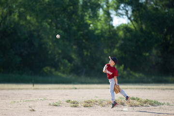 A boy playing baseball throwing the ball across the field