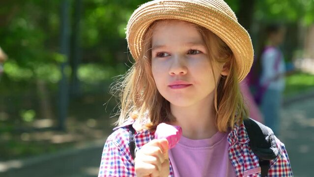 a little blonde girl eats pink ice cream in the park.