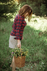 Summer lifestyle portrait of a beautiful young woman smiling and holding a basket with a bouquet of wild flowers. The concept of happiness and love