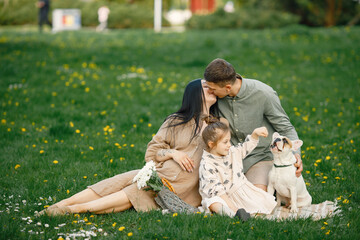 Pregnant mother and her little daughter and husband sitting on a grass in a park