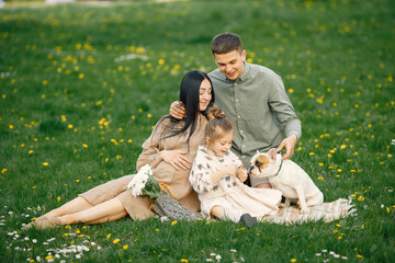 Pregnant mother and her little daughter and husband sitting on a grass in a park
