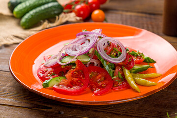 Vegetable salad with tomatoes, cucumbers and red onion on wooden table
