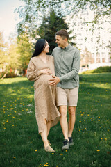 Fototapeta premium Pregnant woman and her husband standing in a park on a grass and hugging