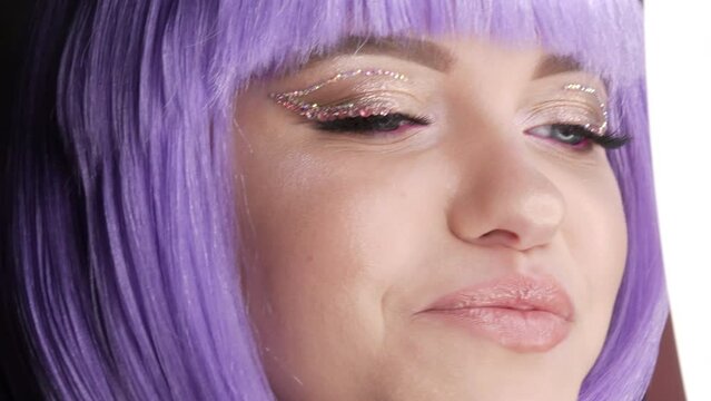 Beautiful young girl model posing in a purple short bob wig, rhinestones on her eyes and stylish pink makeup, high fashion. Face close up