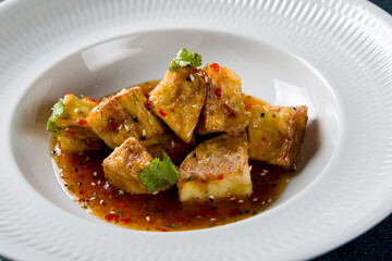 fried eggplant in sweet sour sauce on white plate macro close up