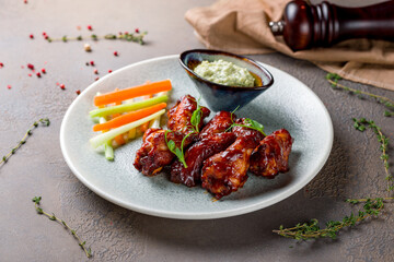 chicken wings in barbecue sauce on plate with blue cheese sauce on brown stone table