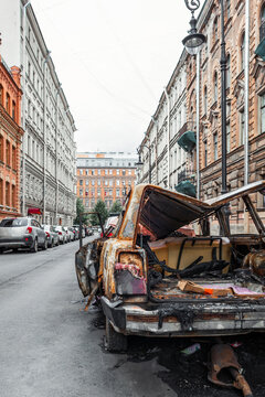 A burnt-out, rusted-out car on the street of a European city, vertical photo