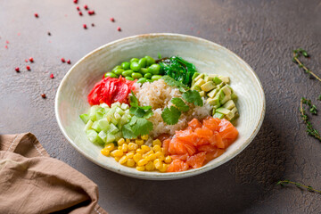 Poke with salmon, rice, avocado, corn, chukka, cucumber, tomatoes and edamame on brown table