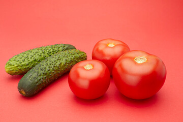 Two cucumbers and three tomato isolated on red background.