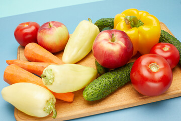 Close up view of vegetables and fruit  on wooden cutting board over on blue background.