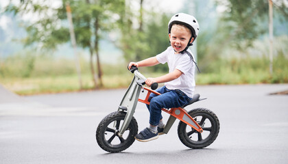 Happy child riding balance bike. Male toddler kid in helmet learning to ride on run bicycle at...