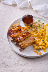 Fried pork ribs in a sauce with French fries, mung bean salad, cabbage, fried onions and sauce