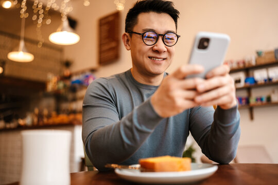Adult asian man using cellphone while having breakfast in cafe indoors
