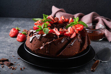 Dark Chocolate Bundt Cake with Ganache Icing and strawberry on dark stone or concrete table background. Festive cake. Selective focus
