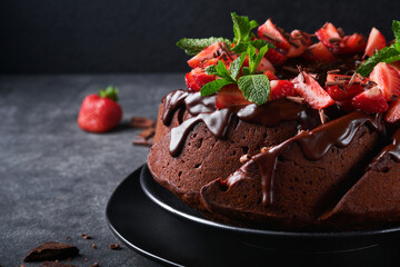 Dark Chocolate Bundt Cake with Ganache Icing and strawberry on dark stone or concrete table background. Festive cake. Selective focus