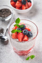 Chia strawberry pudding. Healthy vegan breakfast chia seeds pudding with fresh berries and mint in glass on gray concrete background. Concept of healthy eating, dieting, fitness menu. Selective focus.
