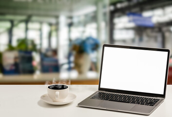 Fototapeta premium A blank white screen laptop and coffee cup are placed on a white desk in an office. The Concept for business, technology, internet, design, and art. Closeup, selective focus, blurred background