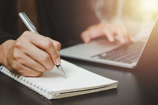 person man holding pen write plan or idea on book with computer laptop on desk.