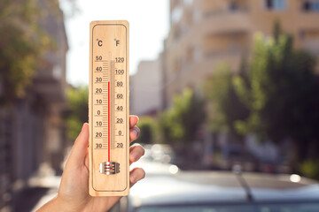 Hot weather. Thermometer in front of an urban scene during heatwave.