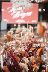 Delicate floral decoration of a wedding banquet of orange, white and red flowers and white burning candles.