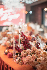 Obraz na płótnie Canvas Delicate floral decoration of a wedding banquet of orange, white and red flowers and white burning candles.