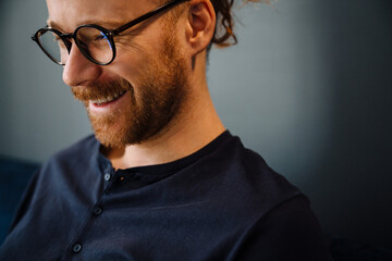 Young ginger man wearing eyeglasses smiling while resting on sofa