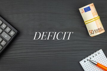 DEFICIT - word (text) and euro money on a wooden background, calculator, pen and notepad. Business concept (copy space).