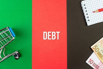 DEBT - word (text) and euro money on a table of different colors, a trolley, a basket of grocery notepad and a red pencil. Business concept, buying, selling, supermarket, store (copy space).