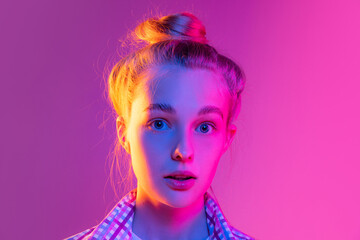 Obraz premium Closeup face of young surpised girl, student looking at camera isolated on magenta color background in neon light. Concept of beauty, art, fashion, emotions