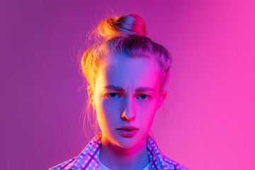 Portrait of adorable young girl, student with wearing plaid shirt isolated on magenta color background in neon light. Concept of beauty, art, fashion, emotions