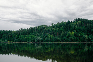 Obraz premium Green mixed forest by the lake in the reflection of the water. Calm natural landscape