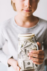 Caucasian teenager boy holding jar piggy bank with money dollars in his hands. Kid save money Saving money for education learning hobby in the future. Teaching child financial literacy with money