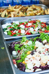 Fried potatoes and salads with vegetables in metal tray at street food festival