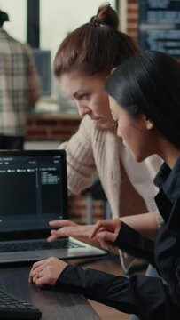 Vertical video Team of software developers talking about source code running on laptop screen while sitting at desk artificial intelligence server room. Database admins collaborating on data coding