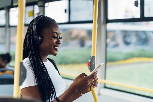African american woman riding a bus and using a smartphone and headphones