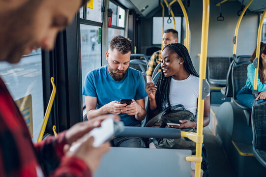 Multiracial friends talking and using a smartphone while riding a bus in the city