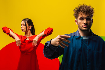 curly man and stylish woman holding glass of different shapes isolated on yellow.