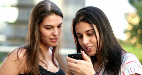 Women using smartphone outside. Female friends checking cellphone screen
